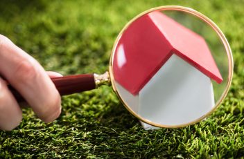 Businessperson Looking At House Model Through Magnifying Glass